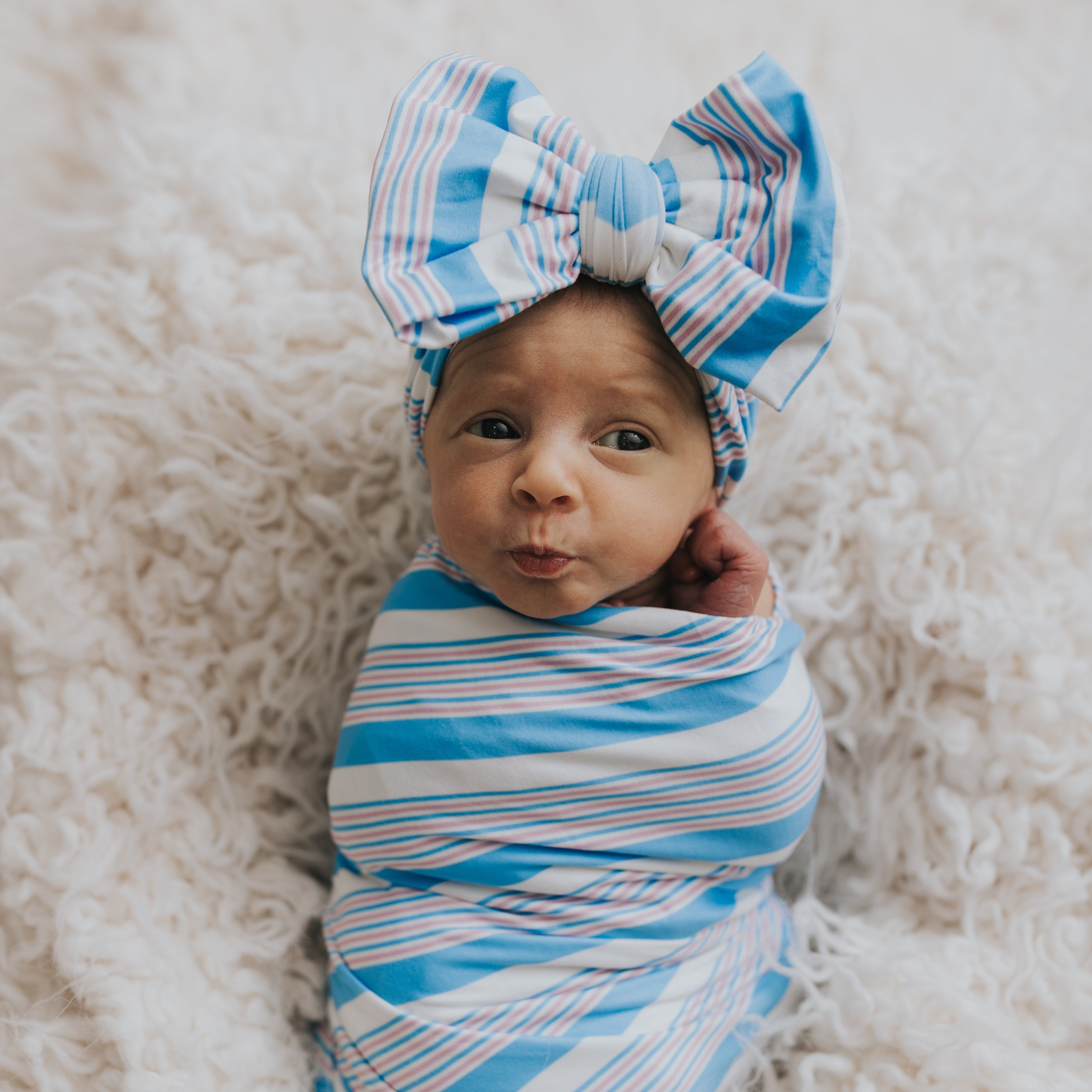 A newborn baby wrapped in a blue and white striped swaddle blanket, wearing a matching hat with a bow.
